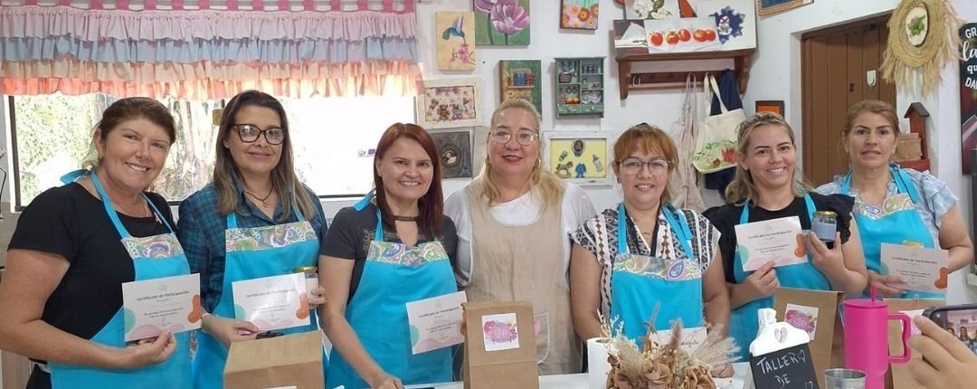 Grupo de alumnas con delantal turquesa mostrando sus certificados al finalizar un taller en La Casita del Arte
